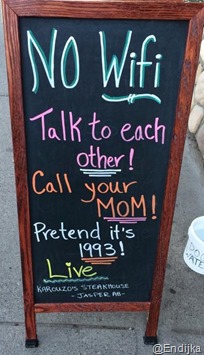 foto di una lavagna all’entrata di un bar, con le scritte NO WiFi. Talk to each other! Call your mom! Prentend it’s 1993! Live!