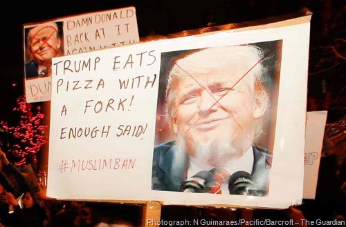 Cartello con foto di Trump con espressione scimmiesca su cui è stata tracciata una X e scritta TRUMP EATS PIZZA WITH A FORK! ENOUGH SAID! #MUSLIMBAN