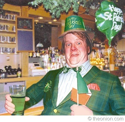 foto di uomo con capelli rossi alticcio che indossa giacca verde, ha in una mano una pinta di birra verde e nell’altra una bandierina irlandese; in testa cappellino verde con scritta St Patrick’s Day 