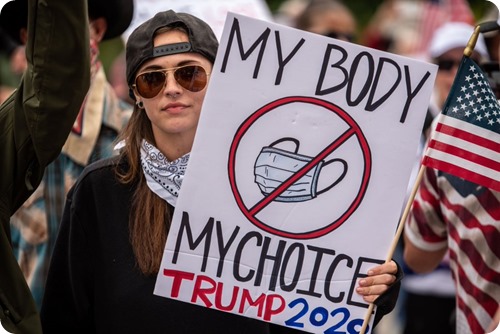 Foto di donna con cartello “My body my choice – Trump 2020” e segno di divieto alla mascherina. 