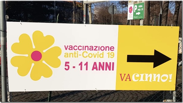 Cartello con primula gialla e scritte “vaccinazione anti-Covid-19 5-11 anni” e freccia con didascalia “VAcinno!”