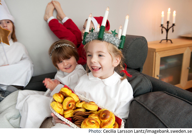 foto di bambina svedese vestita da Lucia con candele in testa e vassoio di Lussekatter